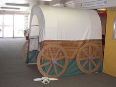 a horse drawn covered wagon sitting in an empty room next to a yellow wall and door