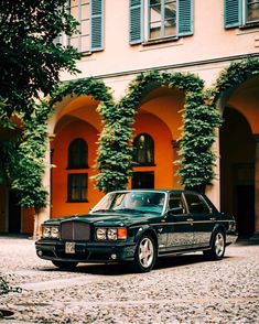 a black car parked in front of a building with ivy growing on it's walls