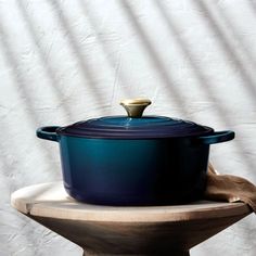 a blue casserole sitting on top of a wooden stand next to a white wall