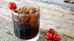 a glass filled with ice and cherries on top of a wooden table