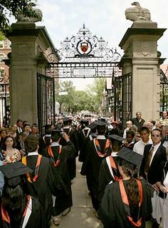 a group of people in graduation caps and gowns walking through an iron gated entrance