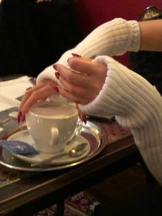 a woman is holding her hand over a cup of coffee on a saucer with spoons