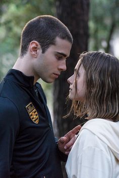 a man and woman standing next to each other in front of trees with their faces close together