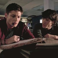 two young men sitting at a table with an open book and pen in their hands