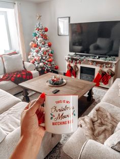 a person holding a coffee mug in front of a living room with christmas tree and couches