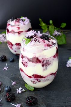 two desserts with berries and whipped cream in them on a black surface surrounded by flowers