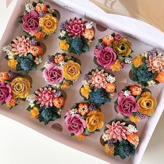 cupcakes decorated with colorful flowers in a white box on a counter top,