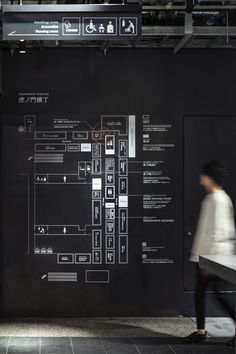 a woman walking past a black wall covered in information