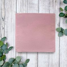 a pink napkin sitting on top of a wooden table next to green leaves and flowers