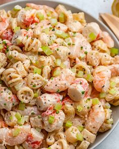 a bowl full of pasta salad with shrimp and celery on the side, ready to be eaten