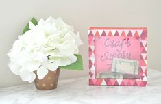 a vase with white flowers sitting next to a pink and white photo frame on a table