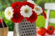 red and white flowers sit in a vase on a table with plates, napkins and utensils