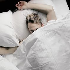 a man laying in bed with white sheets and pillows