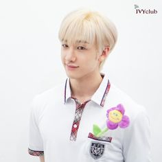 a young man with blonde hair wearing a white shirt and flower decoration on his lapel