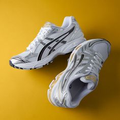 a pair of white and black running shoes on a yellow background