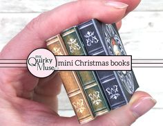 a hand holding three mini books in front of a white wooden background with the words, my quirky miniature christmas books