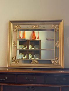 a mirror sitting on top of a dresser next to a shelf filled with plates and cups