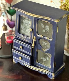 a blue and gold painted wooden cabinet with flowers on the glass doors is sitting on a table