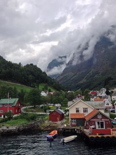 a small village on the water with mountains in the background and clouds hovering over it