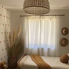 a bed sitting in a bedroom next to a window with white curtains and pillows on top of it