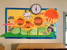 a bulletin board with sunflowers and a clock on the wall above it that says here is the sun