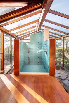 a bathroom with blue tiled walls and wooden flooring, along with large windows that overlook the outdoors