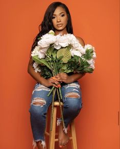 a woman sitting on a stool holding flowers