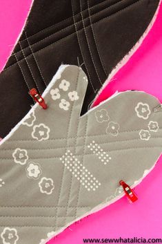 an oven mitt is sitting on top of a pink surface with two pieces of fabric in the shape of hearts