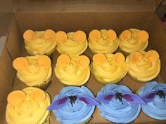 cupcakes with yellow frosting and blue icing are in a cardboard box