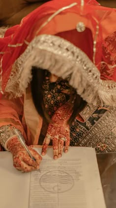 a woman with henna on her hands and writing in a paper while wearing a red headdress