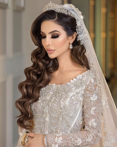 a woman in a wedding dress with long hair wearing a tiara and holding her hand on her hip