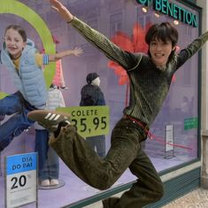 a young boy is jumping in front of a store window with his feet on the ground