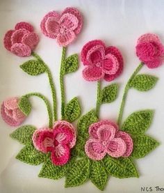 crocheted pink flowers with green leaves on white background