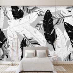 a bed sitting under a wall mounted mural next to a wooden floor covered in white and black leaves