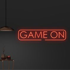 a neon sign that says game on in front of a dark room with a table and chair