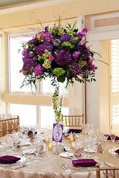 a tall vase filled with purple and green flowers on top of a dining room table