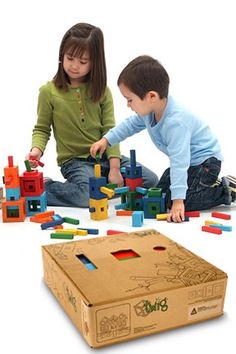 two children playing with blocks and toys on the floor in front of a cardboard box