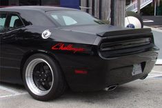 a black car parked in a parking lot next to a tall building with red lettering on it