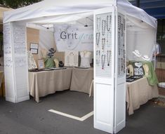 a booth set up for an art show with jewelry on display under a white tent