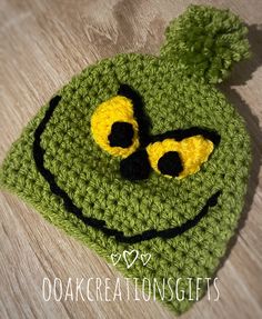 a crocheted frog hat with yellow eyes and black ears on top of a wooden floor