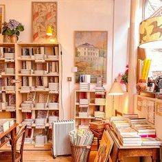 a room filled with lots of books on shelves next to a table and chairs in front of a window