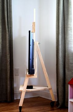 a wooden easel with a television on it in front of a curtained window