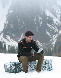 a man sitting on top of a snow covered bench next to a snowy mountainside