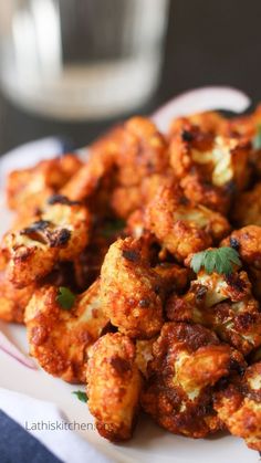 a white plate topped with fried cauliflower next to a glass of water