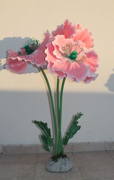 two large pink flowers are in a vase on the ground next to a white wall