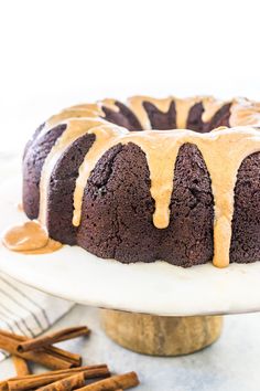 a chocolate bundt cake with caramel icing on a white plate next to cinnamon sticks