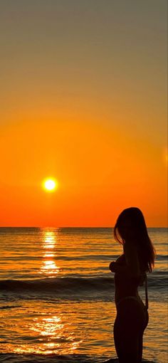 a woman standing on top of a beach next to the ocean under a yellow sun