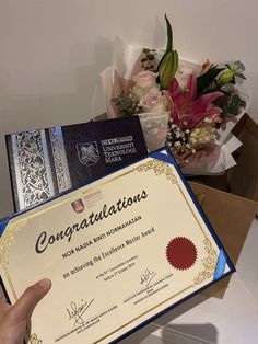 a person is holding up a certificate in front of some flowers and other items on a table