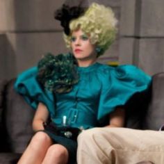 a woman sitting on top of a couch wearing a blue dress and green headpiece