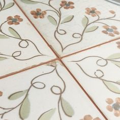 a close up of a tile floor with flowers and vines painted on the tiles in different colors